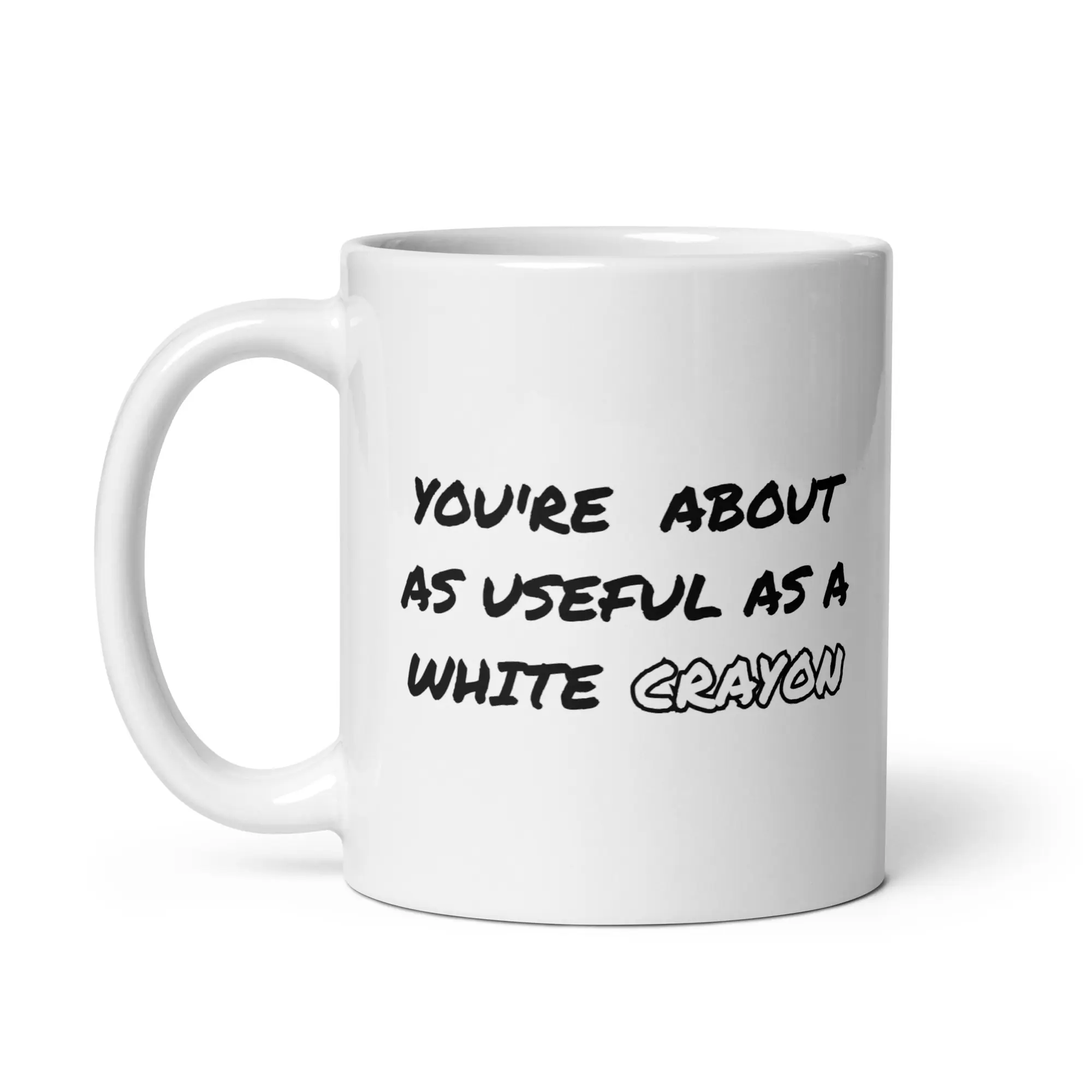 Funny white ceramic coffee mug with black comic-style handwritten text reading "YOU'RE ABOUT AS USEFUL AS A WHITE CRAYON" printed on the side.